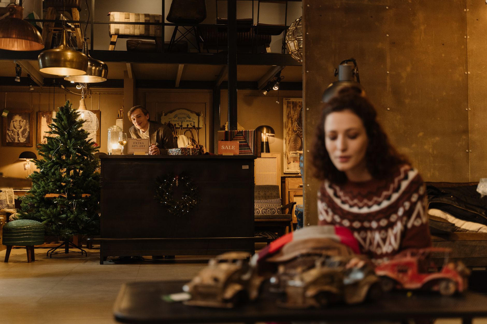 En kvinde sidder ved et bord med legetøjsbiler i en hyggelig butik med juletræ